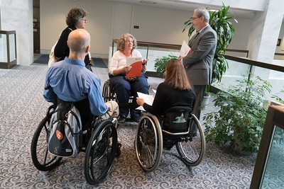 People in wheelchairs and two people standing having a discussion