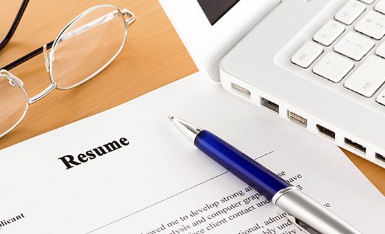 Image of a resume on a table with a pen, eyeglasses and laptop