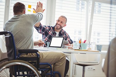 man in a wheelchair high fives man behind desk