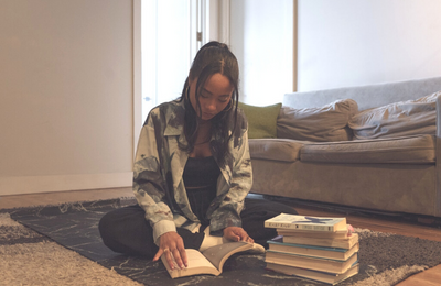 woman sitting on the floor reading a book next to a stack of books
