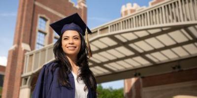 woman outdoors in a graduate robe and hat smiling and looking into the distance