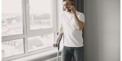 man near a window, leaning on a crutch and talking on a cellphone
