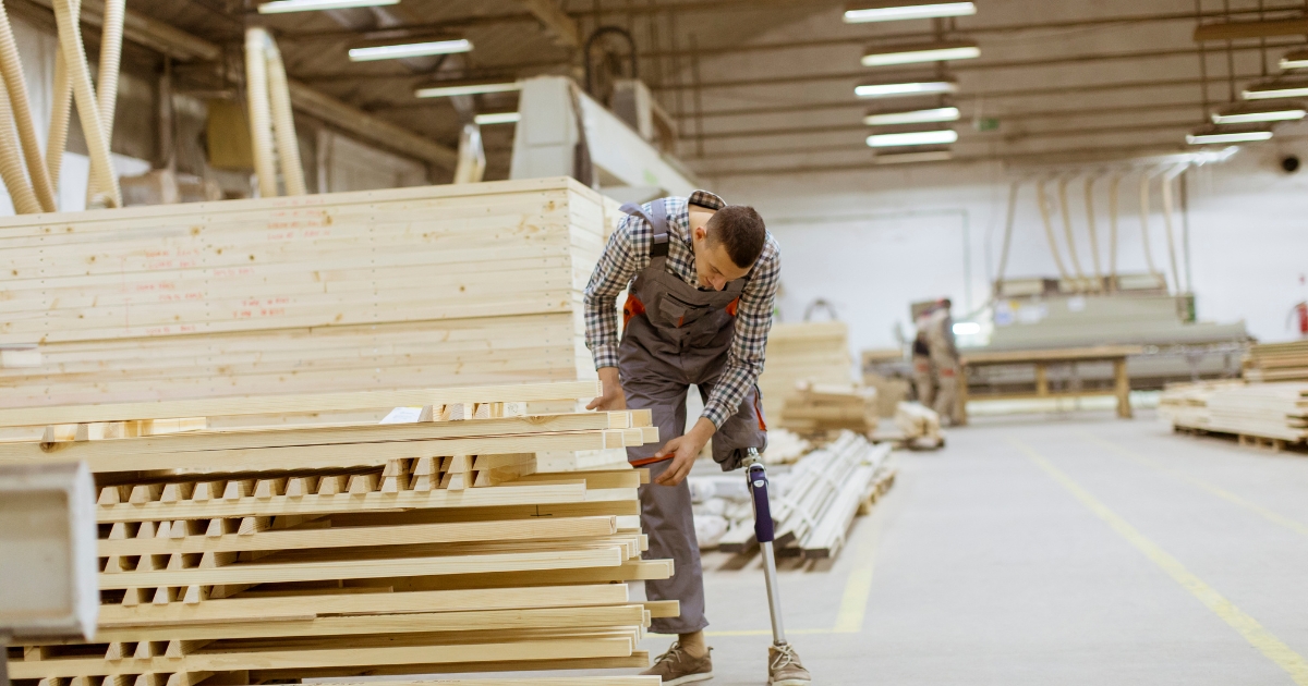 A construction worker, who has a prosthetic leg, is examining wood planks.