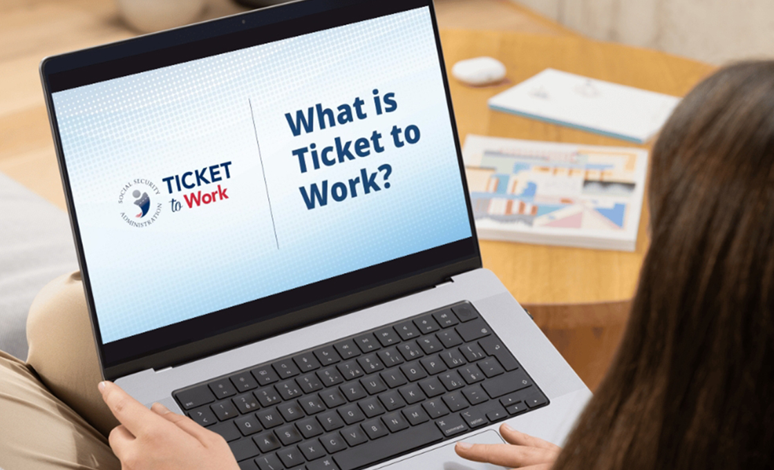 A woman on a laptop facing away from the camera. The laptop screen says 'Ticket to work, what is ticket to work?'