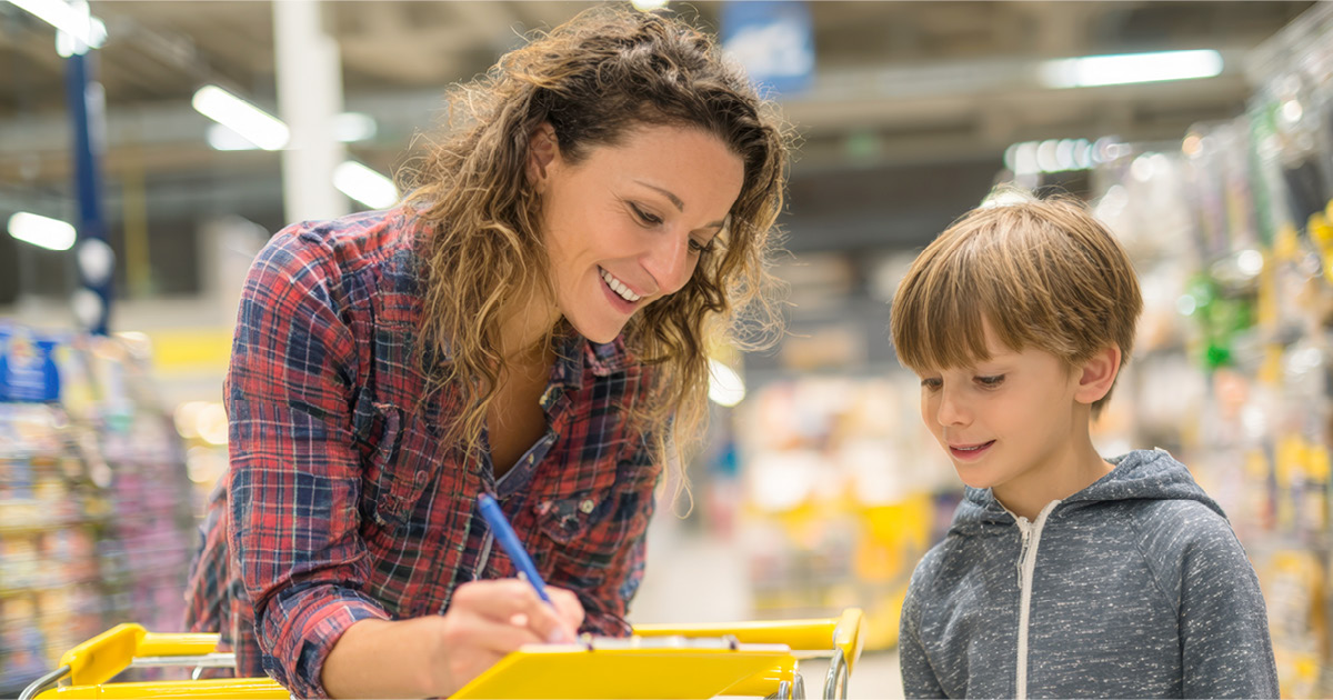 A mother and son looking over a list on a clipboard in a grocery store. 
