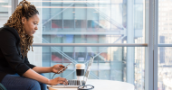 A person sitting at a table using a computer and a smart phone.