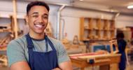 A man wearing an apron in a woodworking shop smiling at the camera